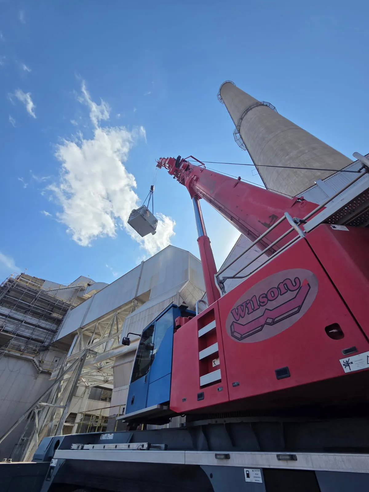 Crane lifting an equipment module at an industrial plant, seen from below beside the concrete stack