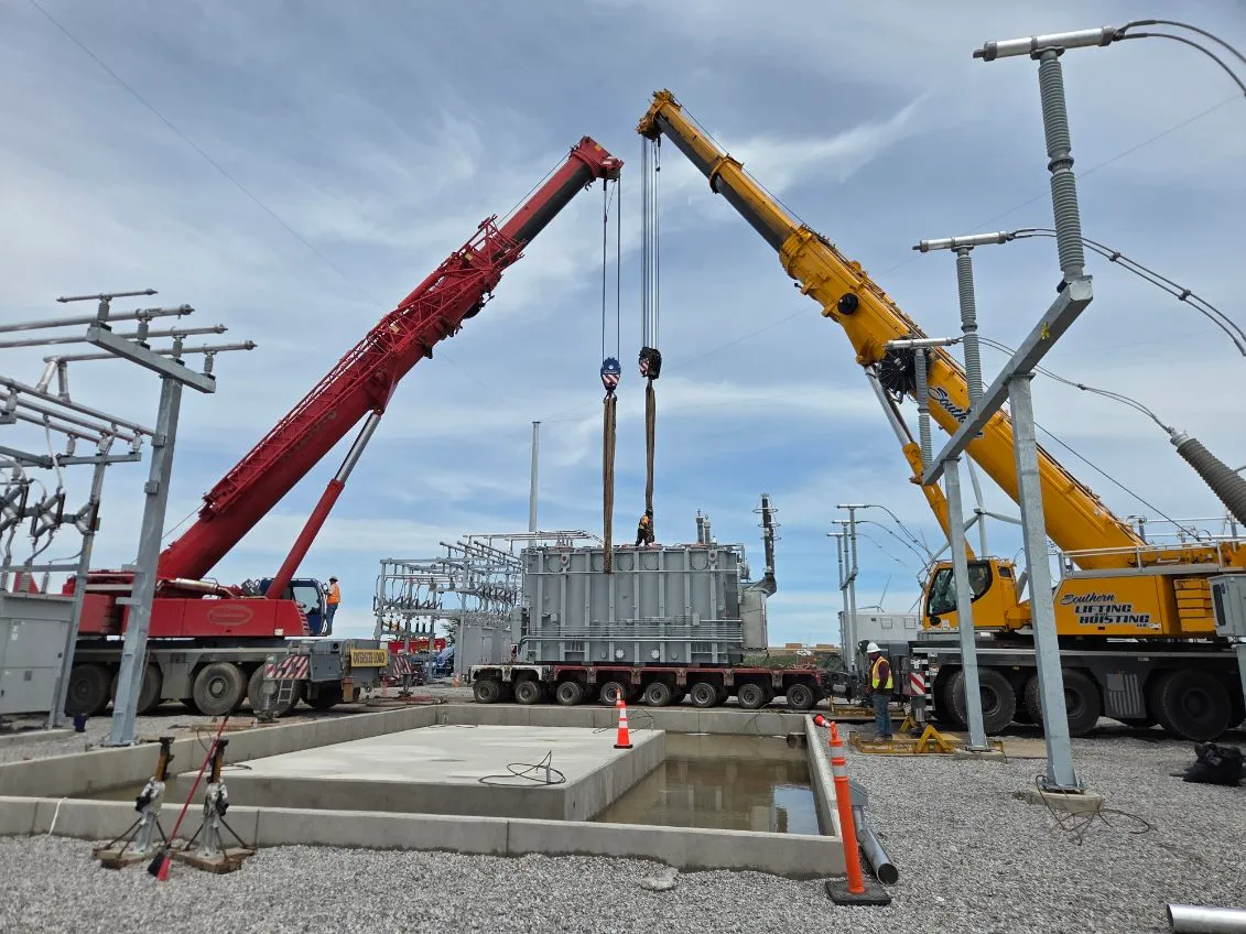 Two cranes working in tandem to lift a power transformer at an electrical substation