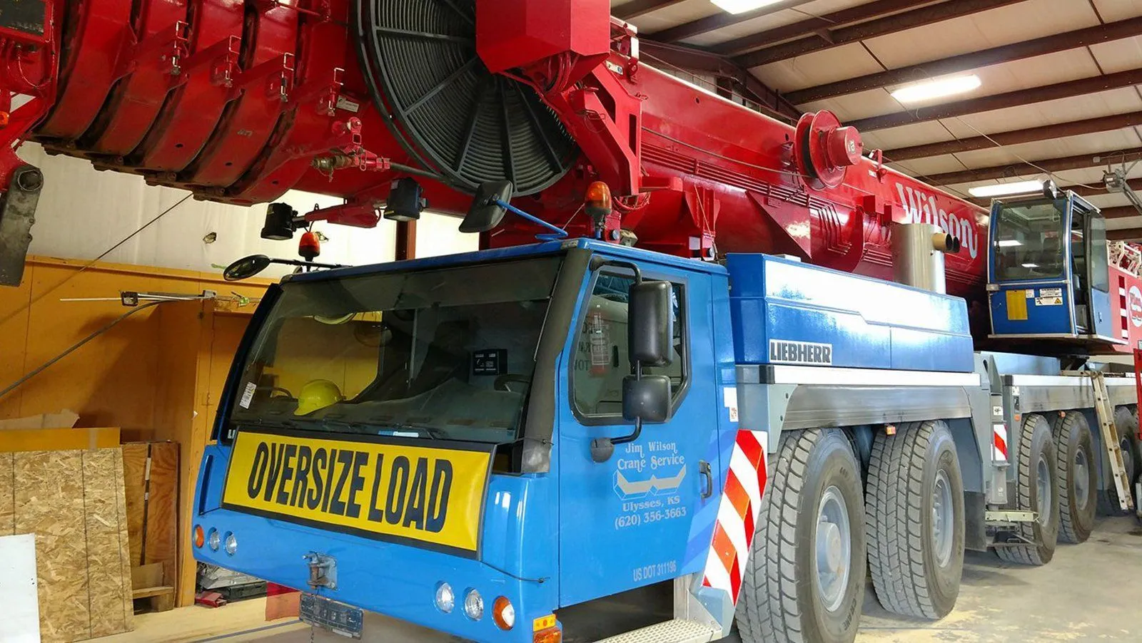 Front of a blue-cab Liebherr all-terrain crane with an oversize load sign, parked inside the shop
